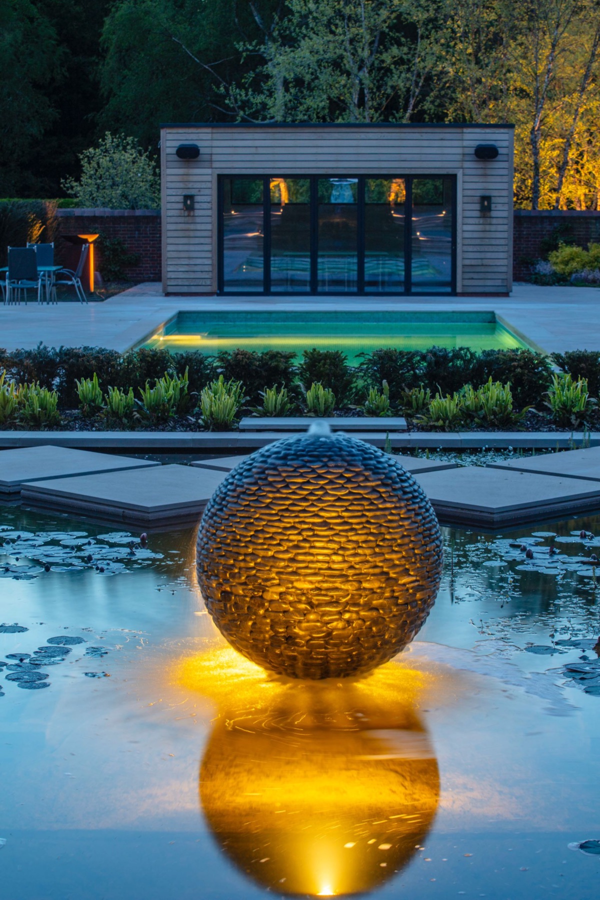 A lit sphere by David Harber in a pool at dusk