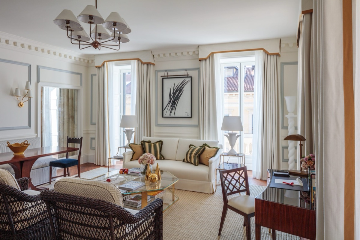A pale panelled drawing room in Milan, lamps lit and the shutters open to the rooftops