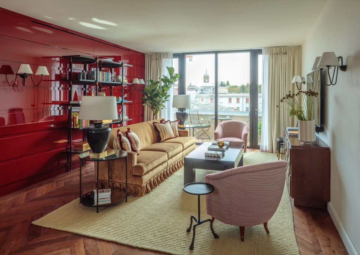 A red-lacquered library wall behind a tan velvet sofa, the windows open over the Milan rooftops