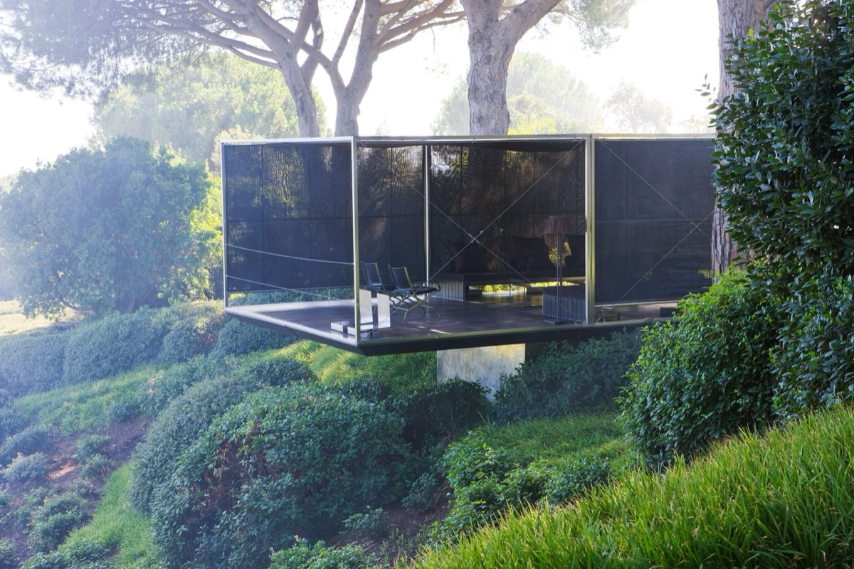 A glass pavilion cantilevered over a wooded hillside, backlit through the pines